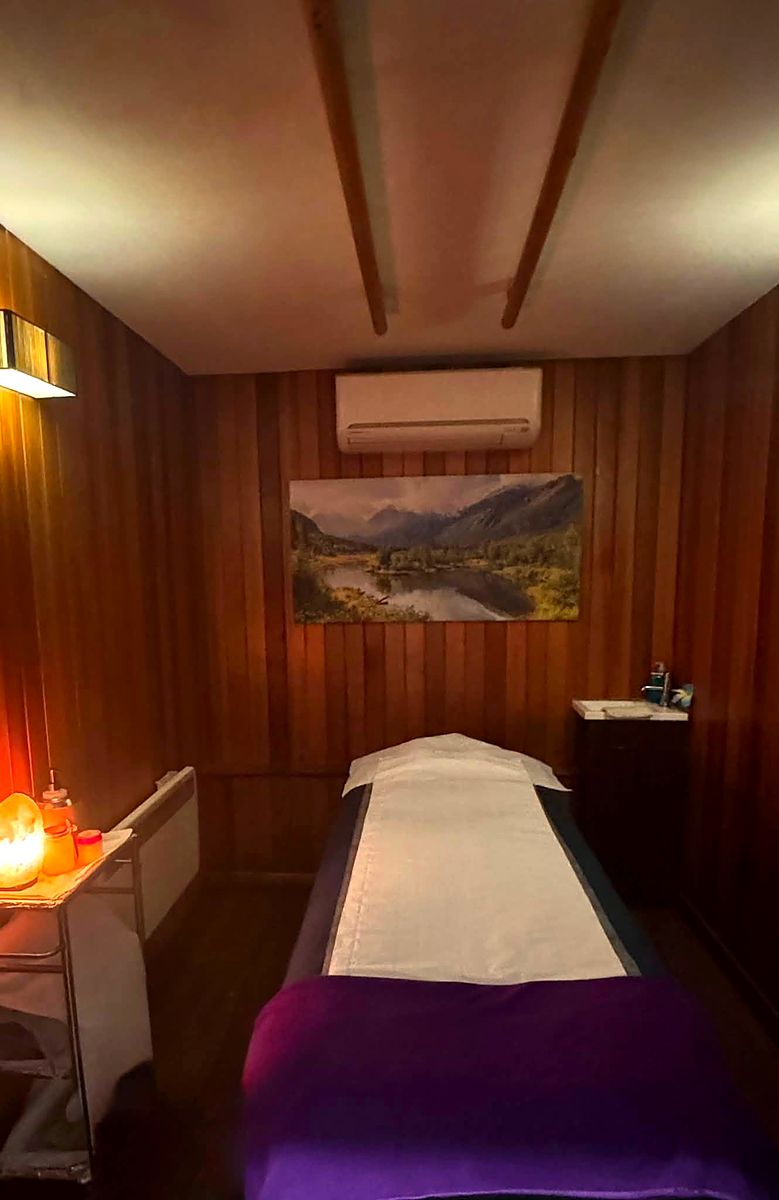 A single treatment room panelled in dark wood, lit by one warm lamp